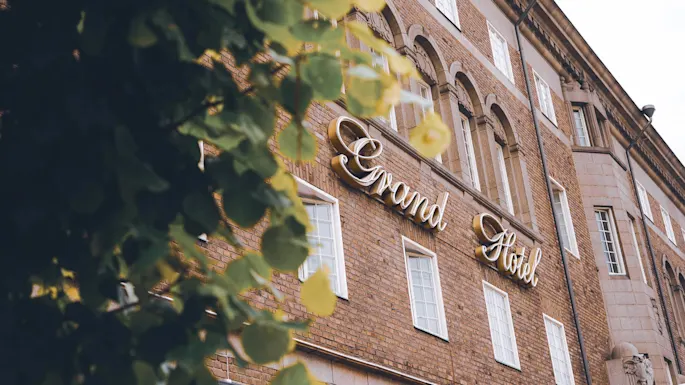 En murstensbygning med skiltet "Grand Hotel", indrammet af slørede blade.