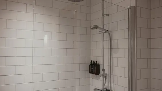 Moderni suihkutila valkoisilla metrolaatoilla, jossa on sadesuihku, käsisuihku ja hygieniatuotteita.