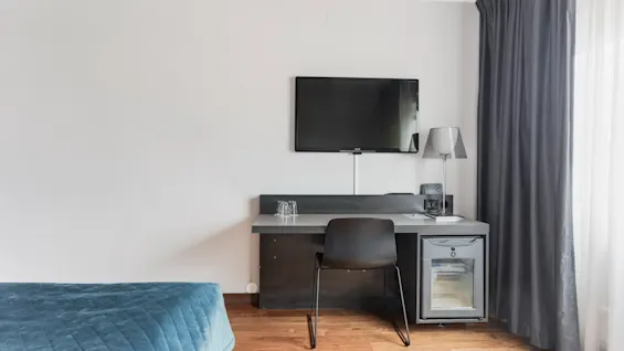 A hotel room with a bed, a desk area with a chair, a wall-mounted TV, and a mini-fridge, offering a comfortable stay.