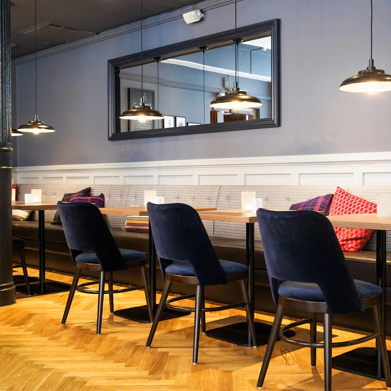 An elegant dining area with plush chairs, lit candles on tables, large mirrors, and pendant lights against muted walls.