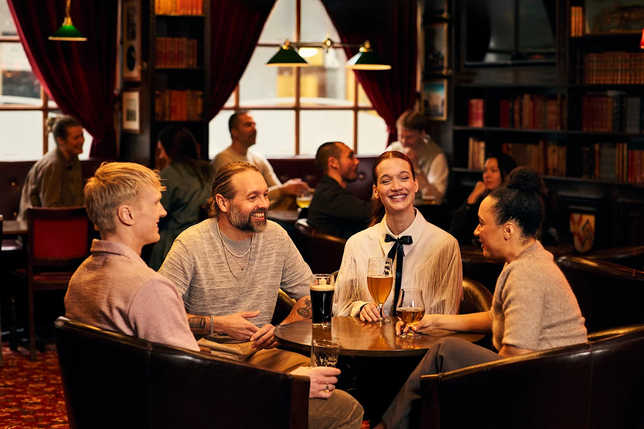 Ystävät nauttivat juomia ja keskustelua lämpimässä, kutsuvassa pubiympäristössä, täynnä naurua ja hyvää seuraa.
