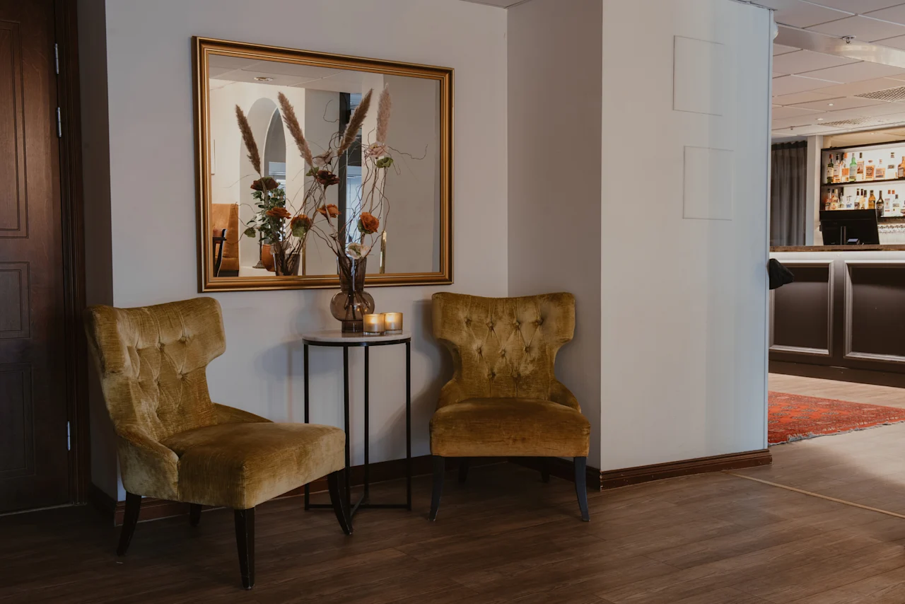 Inviting lounge at Home Hotel Kung Oscar with two plush armchairs, a side table with decor, and a mirror reflecting a bar area.