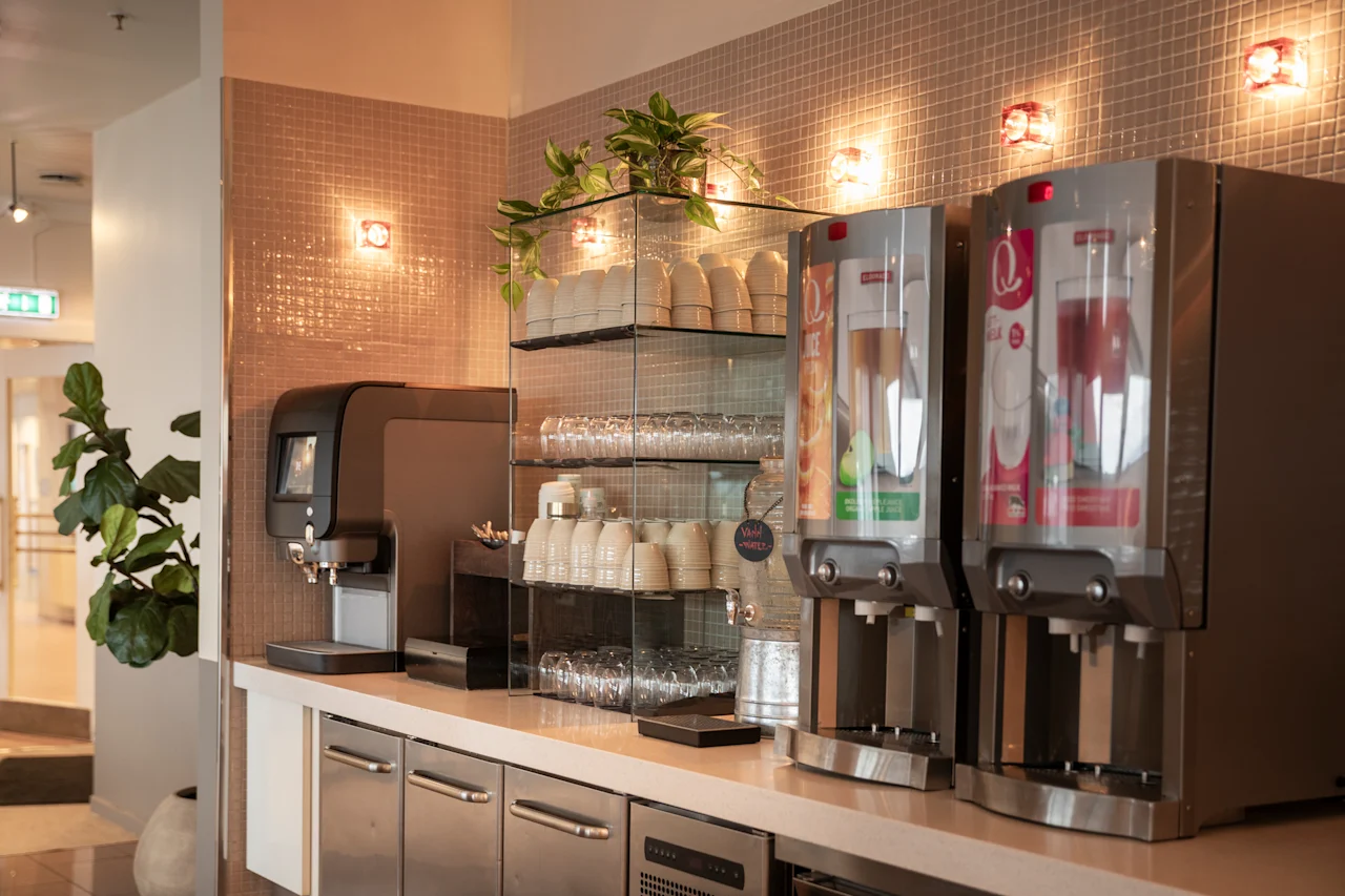 Valoisa itsepalvelujuoma-asema, jossa on kahvi- ja mehuanostelijoita sekä valikoima puhtaita kuppeja ja laseja käyttövalmiina.
