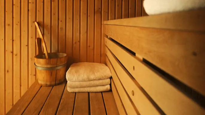 Wooden sauna interior with a water bucket, ladle, and stacked towels on the benches.