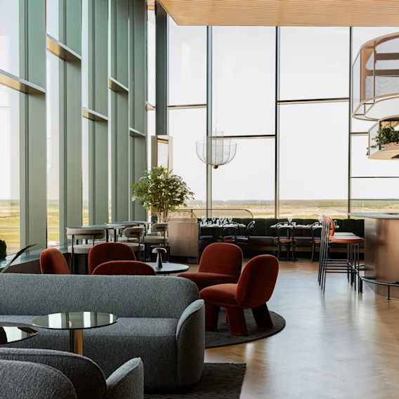 Et moderne hotellounge- og barområde med store vinduer, komfortable sitteplasser og utsikt over naturen.