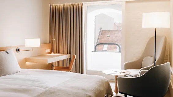 Ett mysigt hotellrum med en bekväm säng, ett funktionellt skrivbord och en avkopplande sittgrupp vid ett ljust fönster.