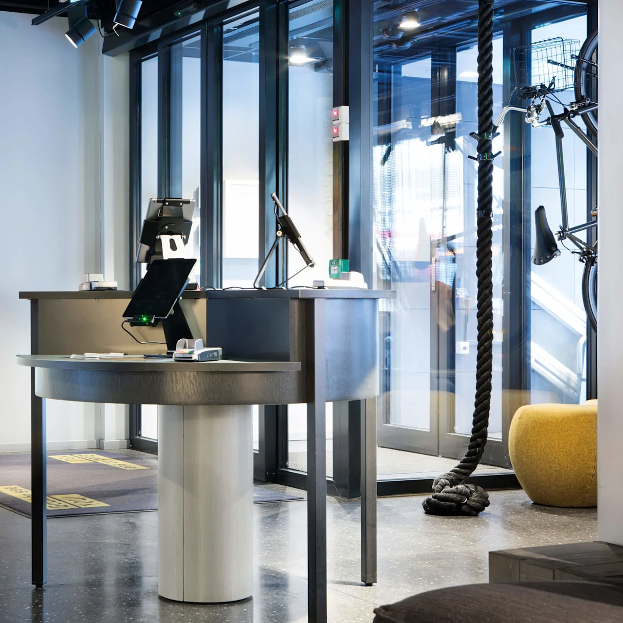 A reception desk with tablets and payment terminals stands in a modern office, adjacent to a large colorful map art on the wall and a glass entrance door.