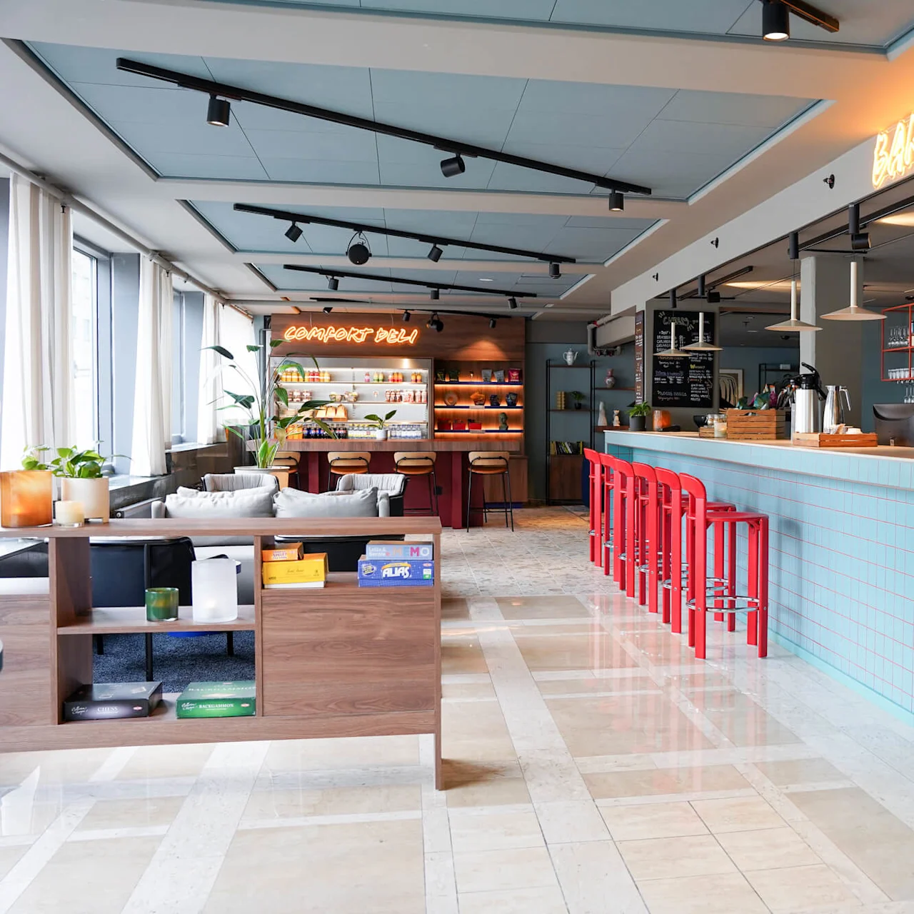 A brightly lit café features a long, blue-tiled counter with red stools and neon signs reading "COMFORT DELI" and "BARCEPTION" amidst a cozy, modern décor.