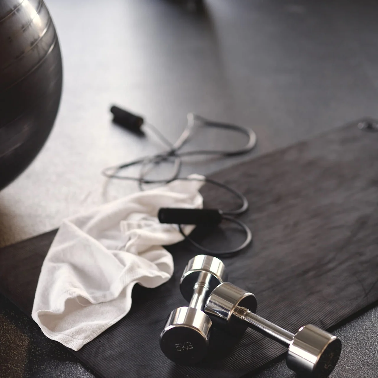A dumbbell and a jump rope rest on a gym floor, suggesting an exercise session in progress.