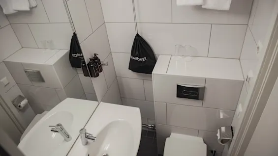 Sink resting below a mirror, complemented by a neatly organized countertop with a toiletry bag and glass, in a tiled, compact bathroom.
