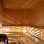 Trebænker beklæder væggene i en varm, lystfyldt sauna. En varmer med sten står i hjørnet og skaber en afslappende atmosfære med sine træpaneler.