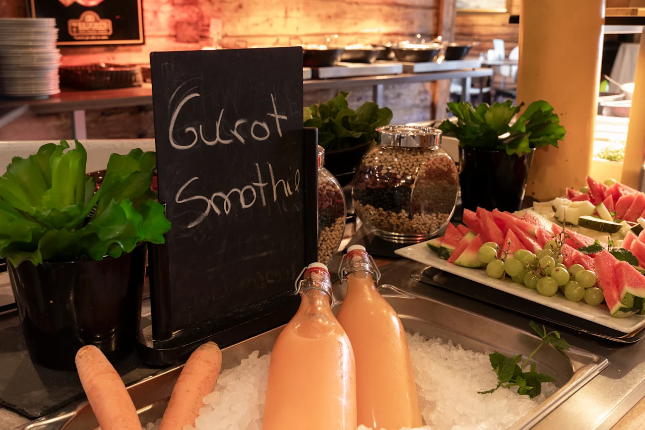 En livlig morgenmadsbuffet med Gulrot Smoothie-flasker på is, frisk vandmelon, druer og forskellige kornprodukter.