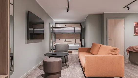 Et moderne rom med en komfortabel oransje sofa, en TV og køyesenger, som skaper et koselig og funksjonelt oppholdsrom.