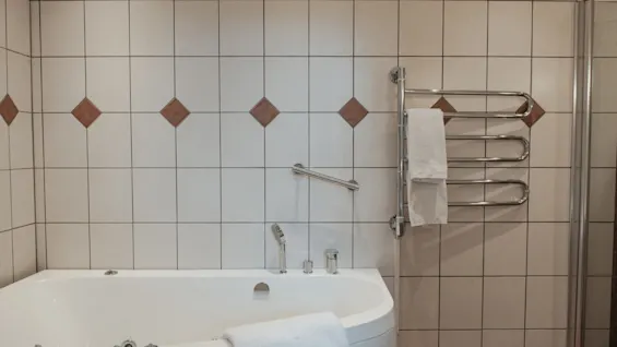 Et rent og innbydende baderom med et hvitt badekar, flislagte vegger og en oppvarmet håndklestativ, klart for et avslappende bad.