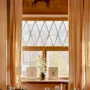 A dining table is set elegantly with glasses and cutlery; behind, a window with beige curtains displays framed art. Above is a mural of a bull with "Oxen" written.