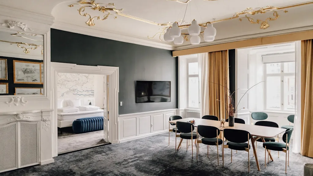 En luksuriøs hotelsuite med spiseplads og udsigt til et soveværelse, med elegant indretning og moderne møbler.