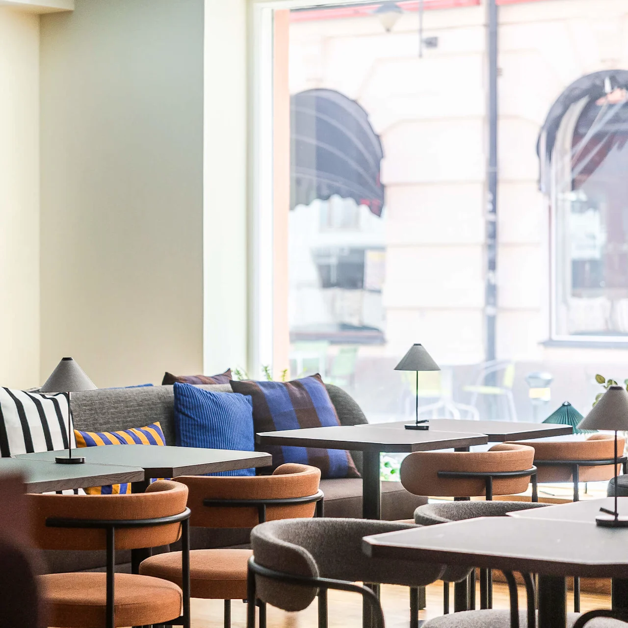 En modern lounge med soffor, kuddar och bord, belyst av naturligt ljus från fönster.