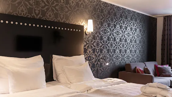 Viihtyisä hotellihuone, jossa on suuri sänky, kuviollinen tapetti ja mukava sohva, kutsuen rentoutumaan.