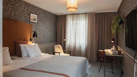 Viihtyisä hotellihuone, jossa on mukava sänky, toimiva työpöytäalue ja lämmin valaistus, täydellinen rentoutumiseen tai työntekoon.