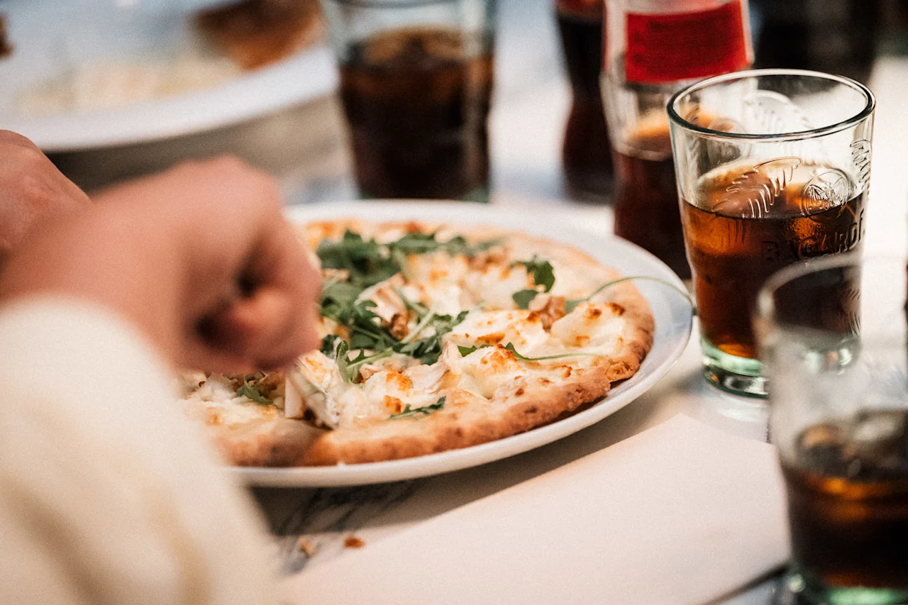 Enjoying a meal with pizza topped with cheese and greens, accompanied by refreshing drinks.
