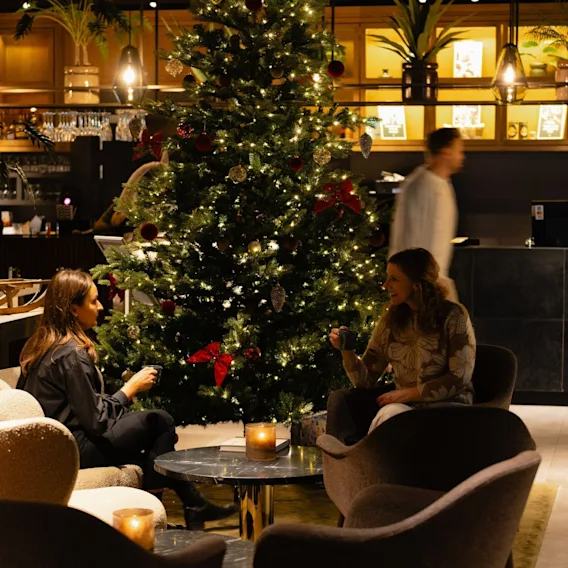 To kvinner drikker kaffe i en hotellobby ved siden av et stort pyntet juletre.