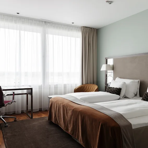 Et moderne og innbydende hotellrom med en koselig seng, en funksjonell arbeidsplass og rikelig med naturlig lys fra et stort vindu.