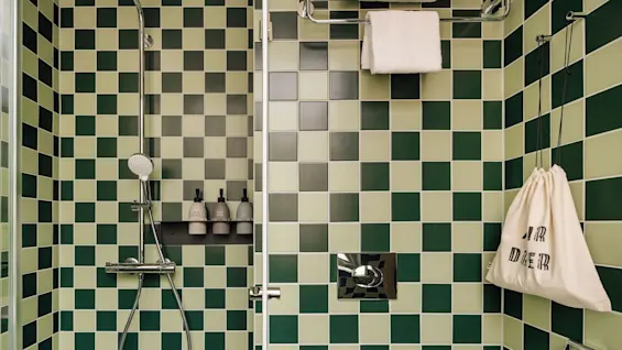 A lively green checkered bathroom at hobo oslo, ready for a refreshing shower. Towels are neatly stacked