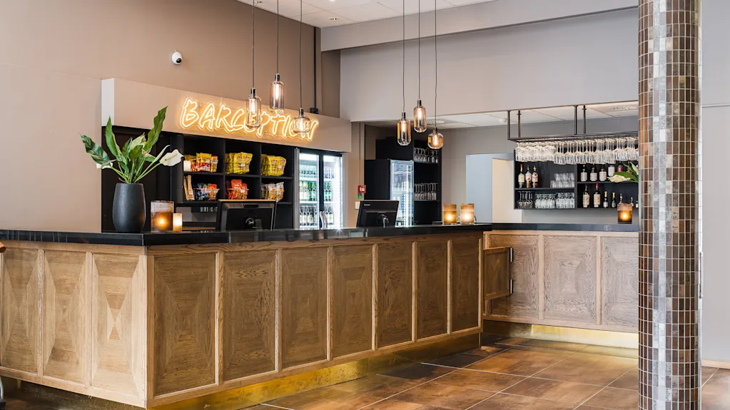 Modern hotel reception and bar in light wood with a glowing Barception sign on the wall.