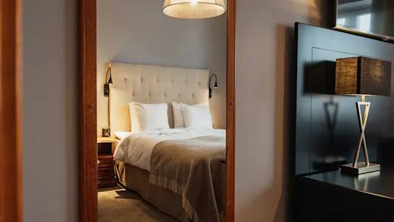 Ett mysigt hotellrum med en bekväm säng speglad i en spegel, med en stilren lampa på ett mörkt skåp.