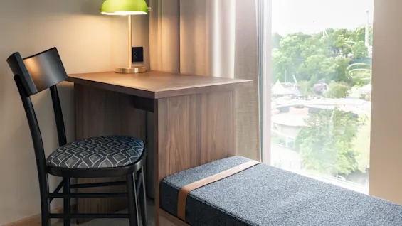 Et koselig skrivebordsområde med en grønn lampe, en stol og en benk ved et vindu med utsikt over et grønt landskap.