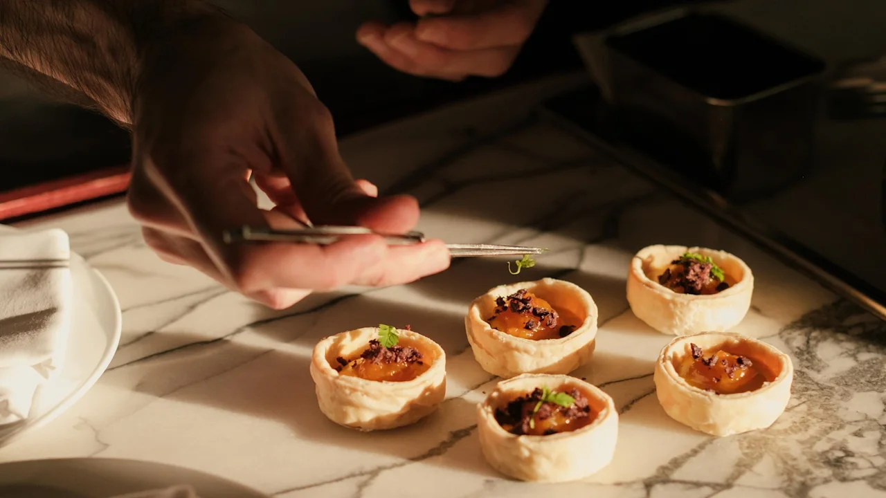En kock garnerar noggrant små pajer med en pincett på ett marmorbord