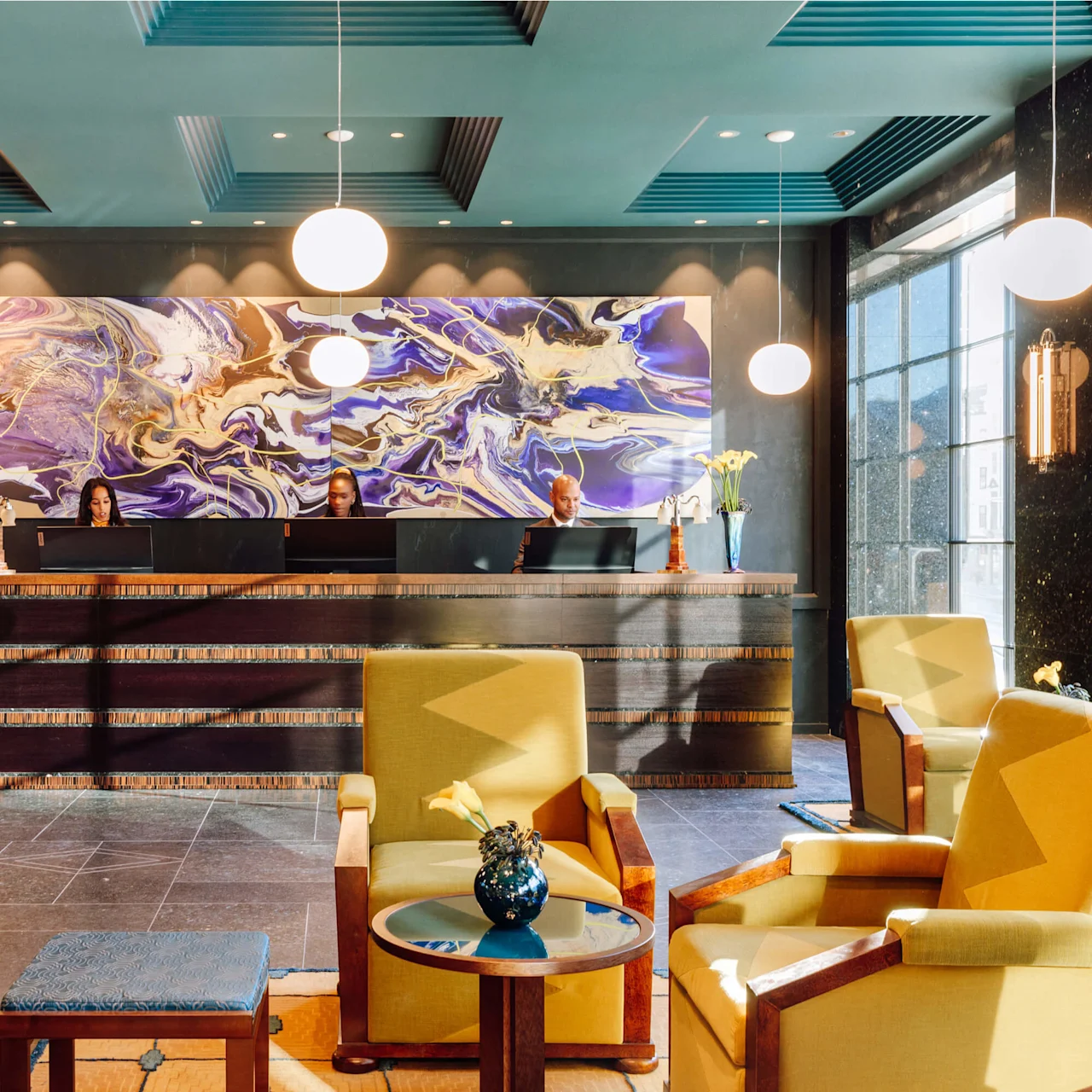 Hotellobby med personale bag receptionsdisken, stort abstrakt kunstværk, siddeområde med lænestole og borde, moderne belysning, i et luksusinteriør.