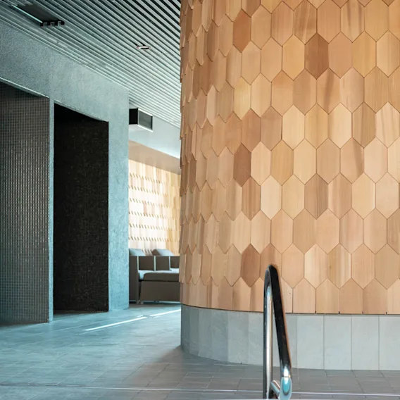 Badkar med metallhandtag står i ett elegant, modernt spa-interiör med sexkantiga träpaneler och grå kaklade väggar, under ett slattak med stämningsbelysning.