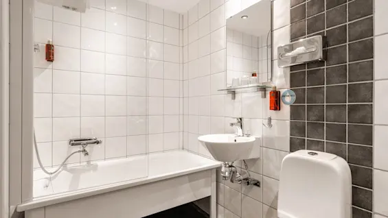 Puhdas ja moderni kylpyhuone Comfort Hotel Linköping Cityssä, jossa on kylpyamme, pesuallas, wc ja säästä vettämme kyltti.