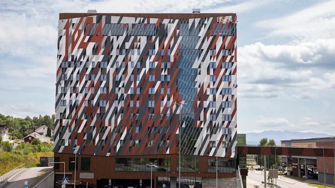 A modern building with a striking red, white, and grey geometric facade, featuring the number 1624 at the top. Cars are on the road below.