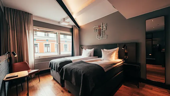 A cozy hotel room with two beds, a window overlooking a city street, and a full-length mirror.