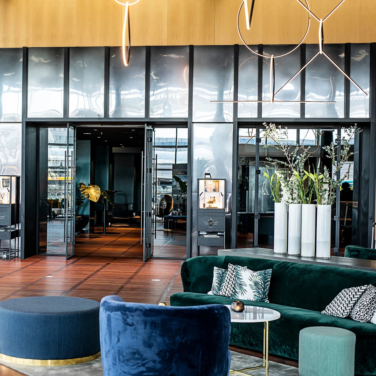 Lyxig hotellobby med mjuka sittplatser och elegant inredning. Stora glasdörrar öppnar upp till en stilfull interiör med växter och stämningsbelysning, vilket skapar en sofistikerad och inbjudande atmosfär.