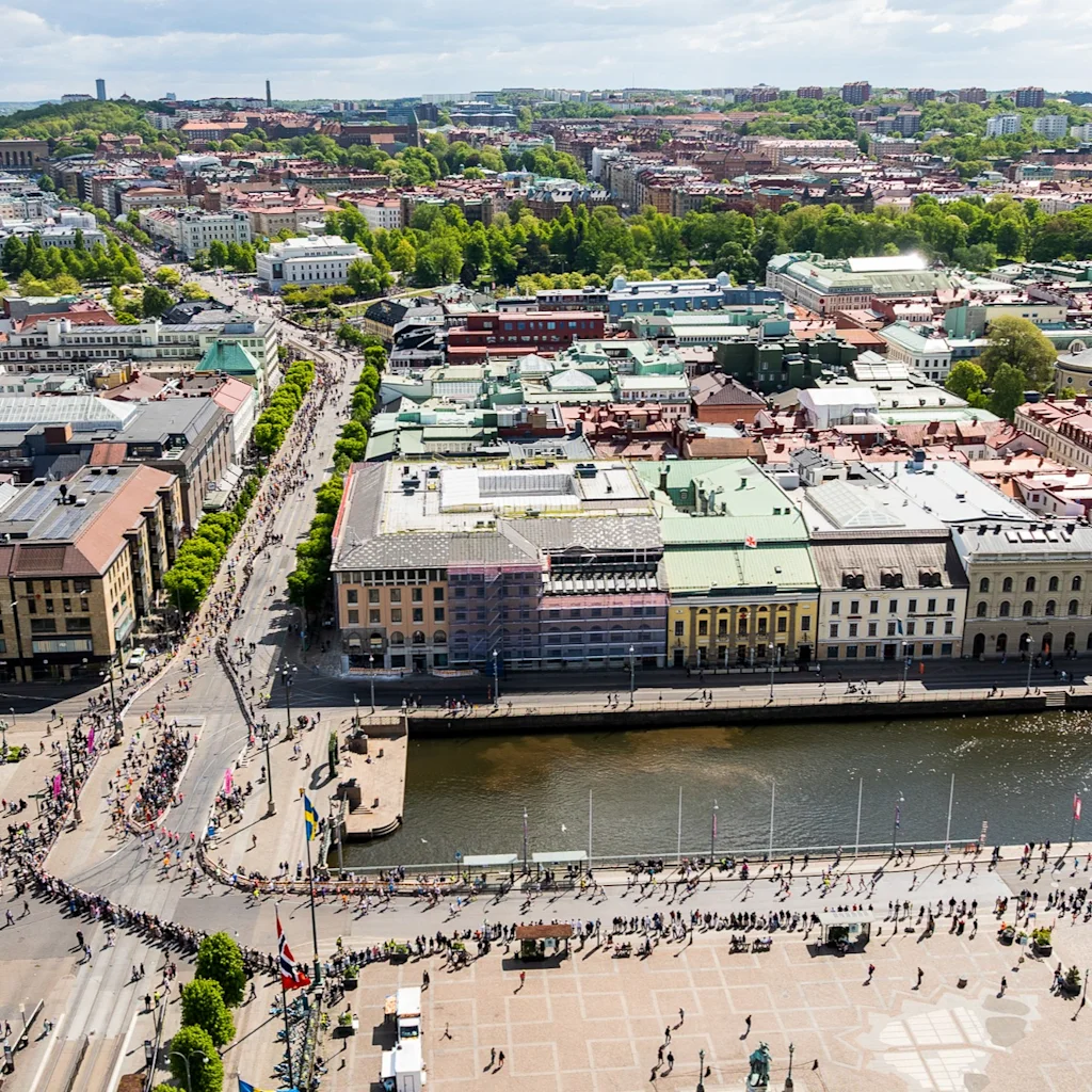 Flygvy över en stad med många människor som deltar i Göteborgsvarvet, ett stort löparevenemang, längs gator och vid en kanal.