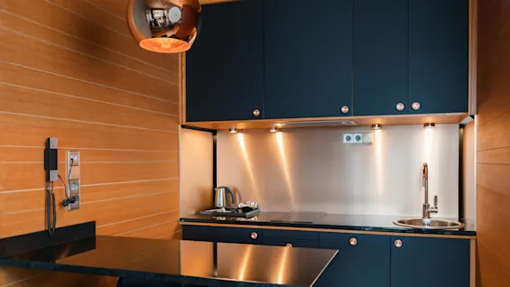 A modern kitchen with wooden walls, dark cabinets, and stainless steel appliances illuminated by under-cabinet lighting.