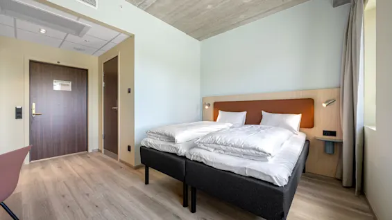 A modern and inviting hotel room featuring two comfortable beds, light walls, and a unique concrete ceiling.