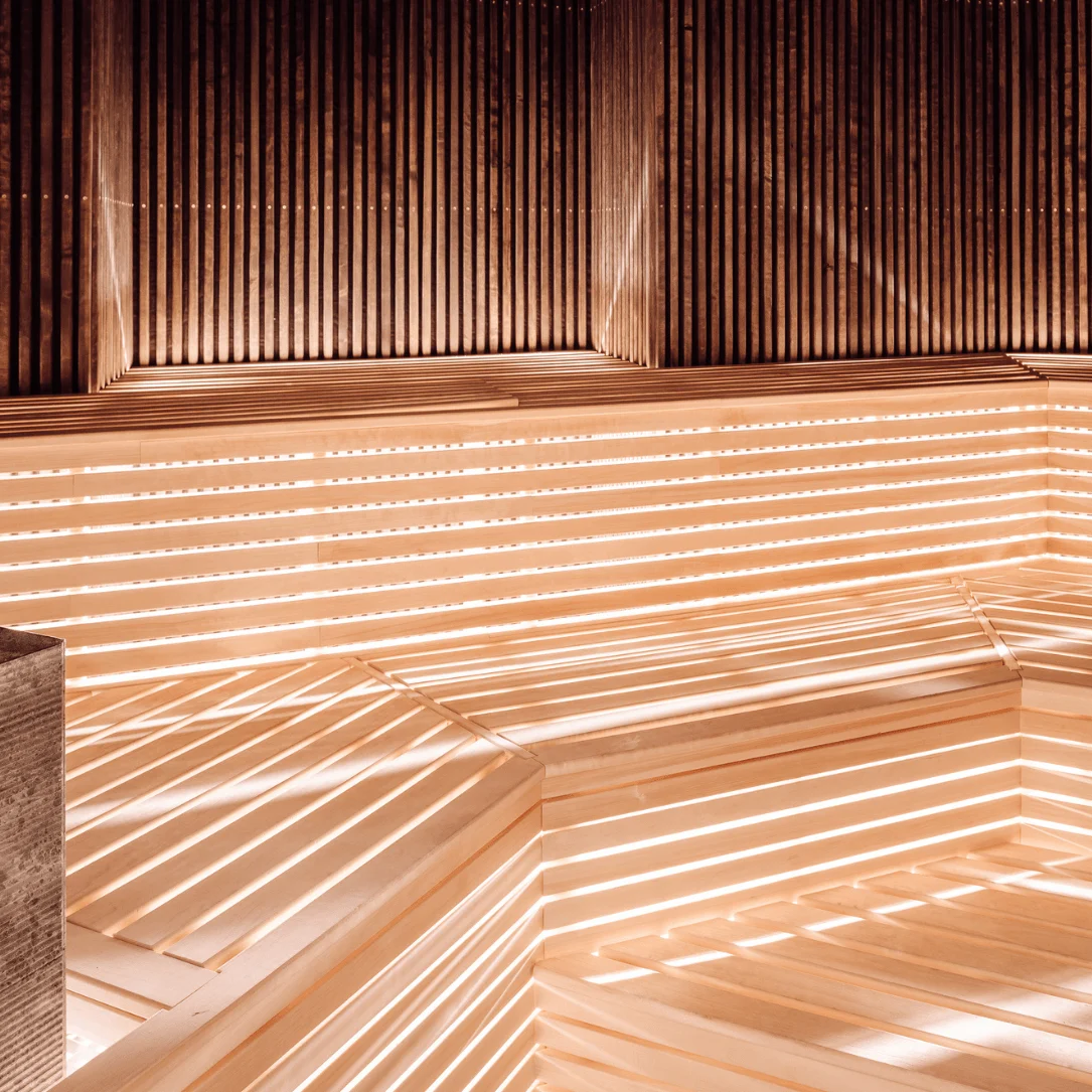 Wooden benches surrounded by vertical slats, illuminated by warm lights, suggesting a cozy sauna atmosphere.