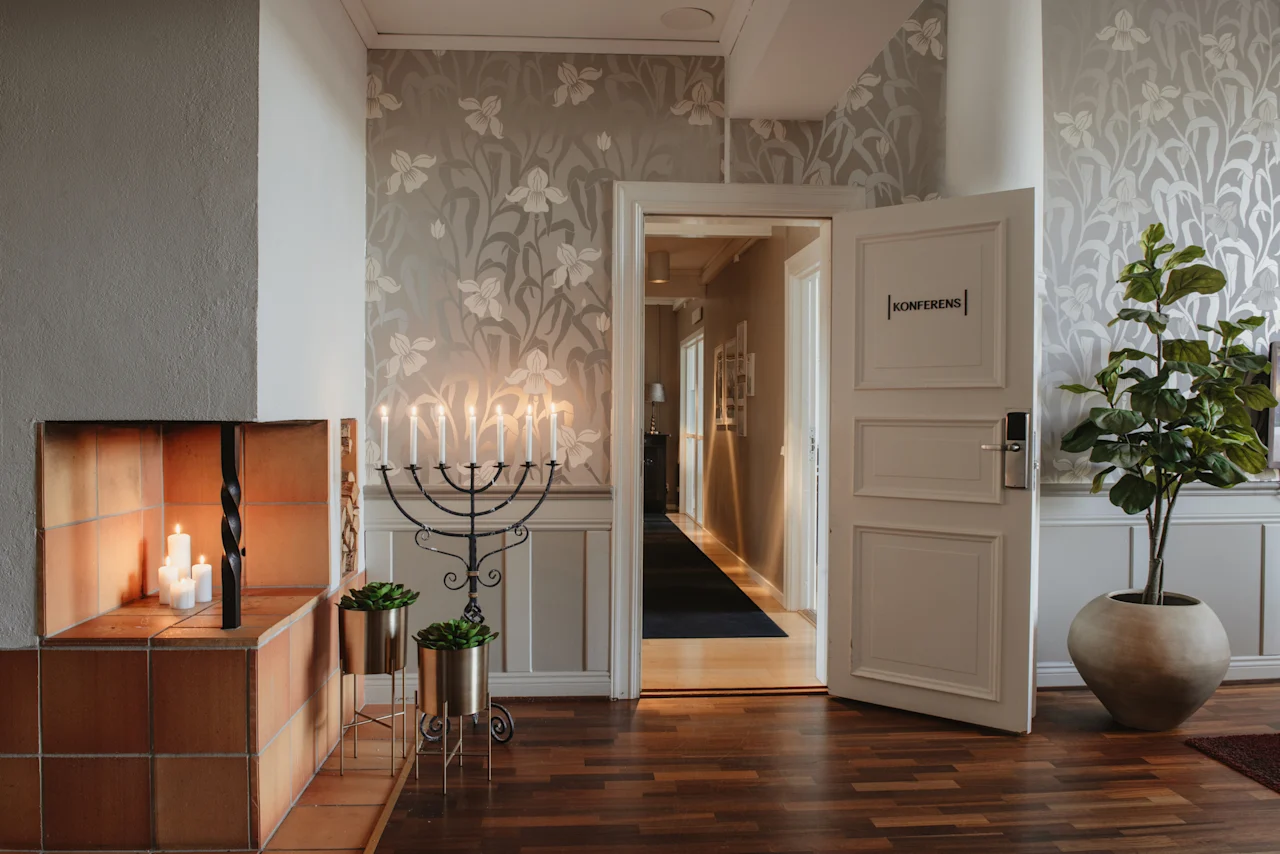 En mysig hotellkorridor med en tänd ljusstake, en öppen spis med ljus och en dörr märkt KONFERENS som leder till ett annat rum.