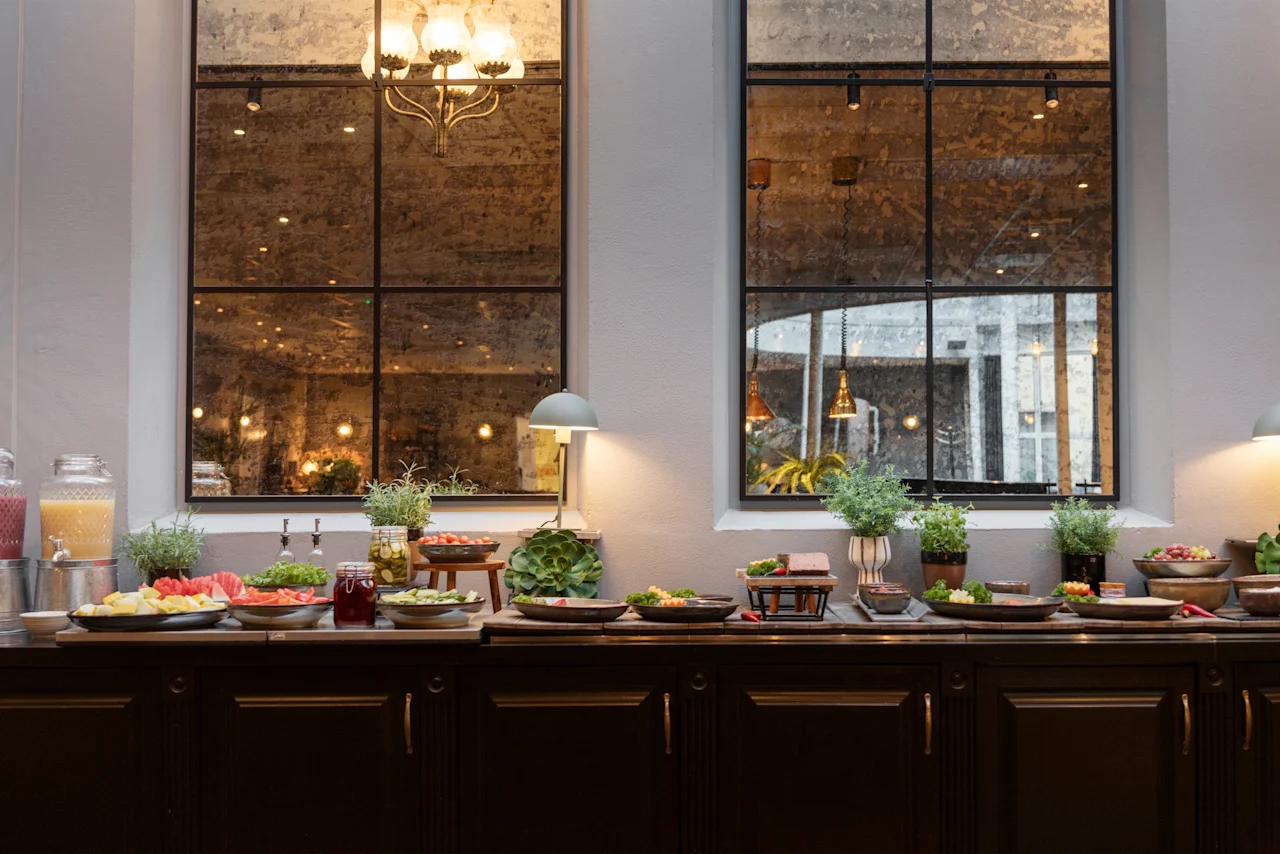A vibrant breakfast buffet at Home Hotel Grand Bodø, featuring fresh fruits, salads, and juices, set against a backdrop of large windows.