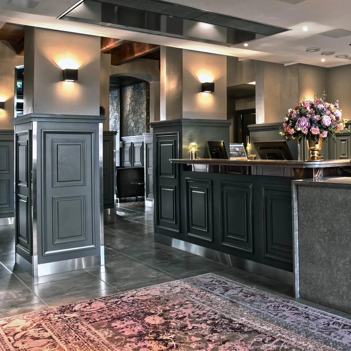 Elegant hotel reception desk with flowers, lit lamps, and displayed beverages, set in a modern and luxurious interior.