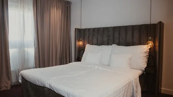 Ett mysigt hotellrum med en stor säng, vita lakan och varm belysning, redo för en bekväm vistelse.