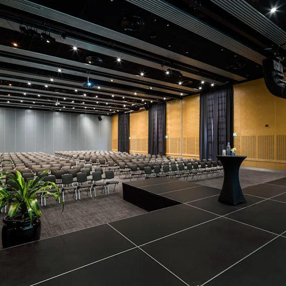 A modern hotel conference room with rows of chairs facing a stage, ready for a presentation or event.