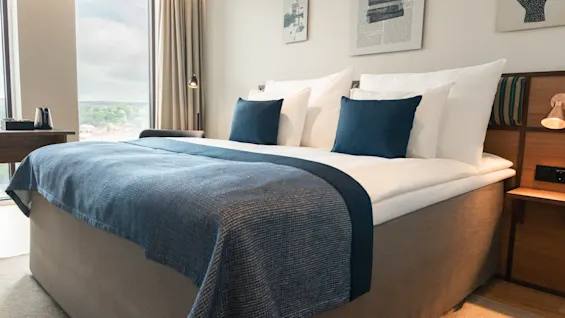 Et komfortabelt hotellrom med en stor seng, blå detaljer og en naturskjønn vindusutsikt.