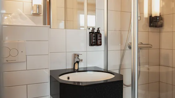 A clean and modern hotel bathroom featuring a sink with a mirror above it and a shower cabin to the side.