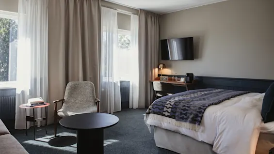 Ett ljust och inbjudande hotellrum med en mysig säng, ett funktionellt skrivbord och en bekväm sittgrupp vid solbelysta fönster.