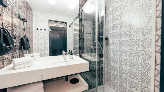 A modern bathroom features a white sink with soap dispensers, set against patterned tile walls. A glass shower and towels provide a sleek aesthetic. Text: "hair d1", "paper".